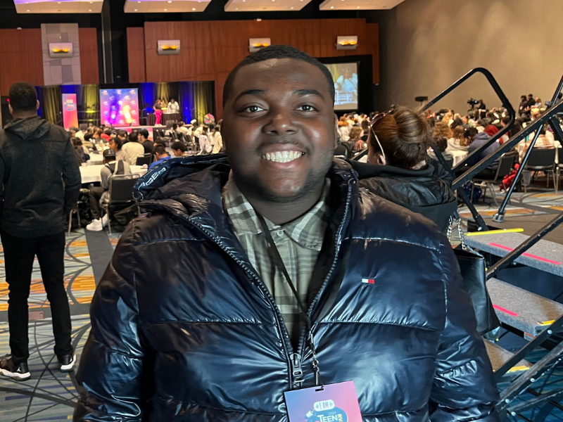 Smiling young man on the floor of a convention wearing a puffy black coat and ID badge