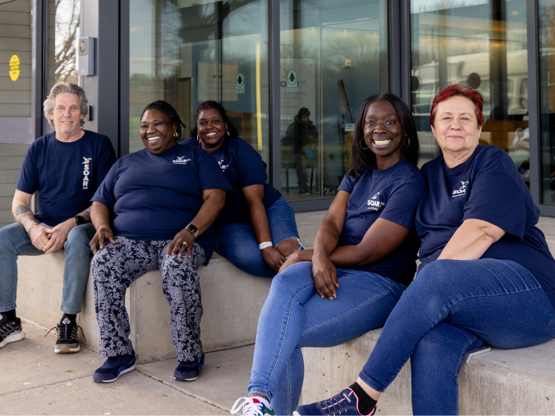 Five Direct Support Professionals (DSPs) seated outside SOAR365's Saunders building.