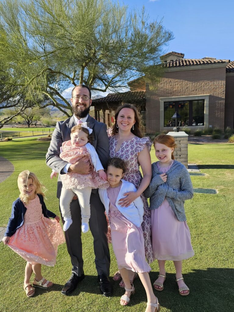 A smiling, outdoor photo of Anna's family - her parents and three older sisters, all dressed up.