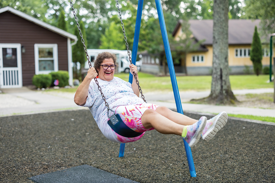 A joyful woman in casual clothes swings on a blue swing set in a park