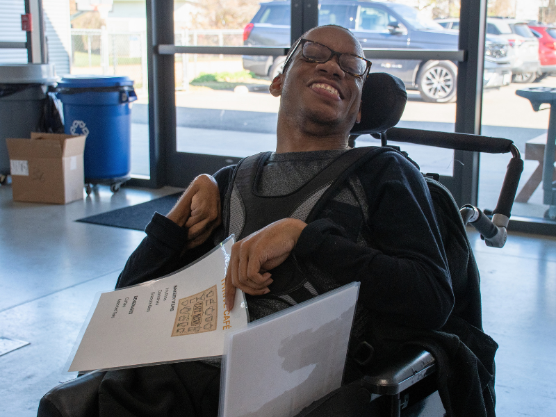 Rashad Adult Day Support Saunders Young man in wheelchair smiles while holding menus