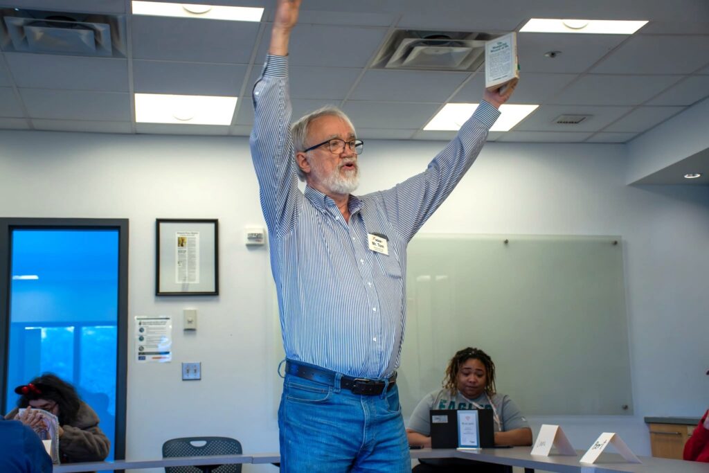 Tom stands with his arms in the air holding a book during a lively reading.