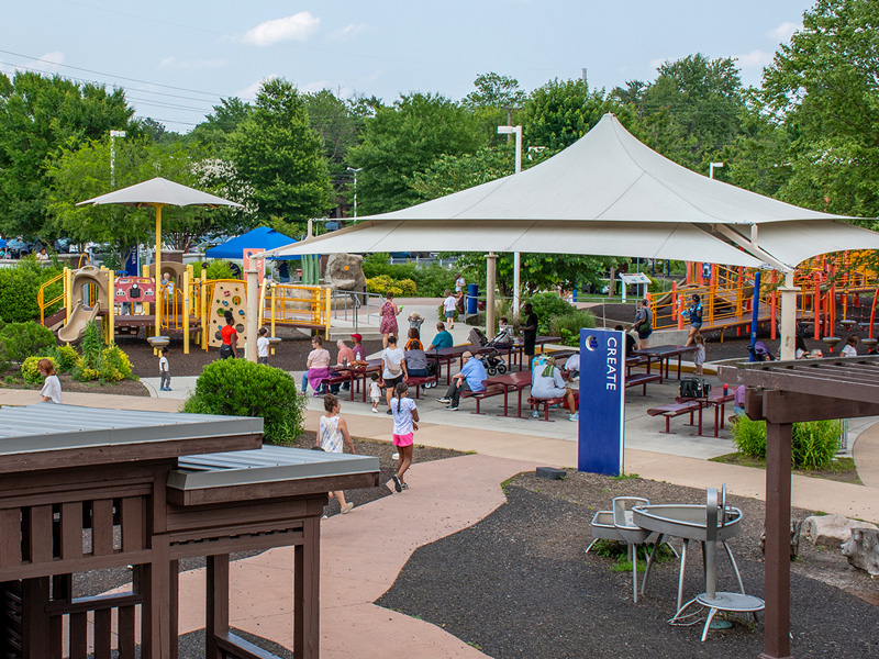 Families enjoy playing on playground equipment and resting in the shade at PARK365.