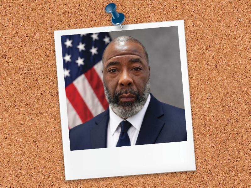 Lonnie A gentleman in a suit and tie poses for a portrait in front of an American flag.