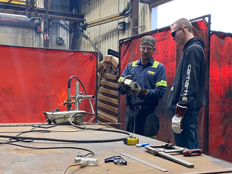 Two men in a workshop discussing how to use power tools.